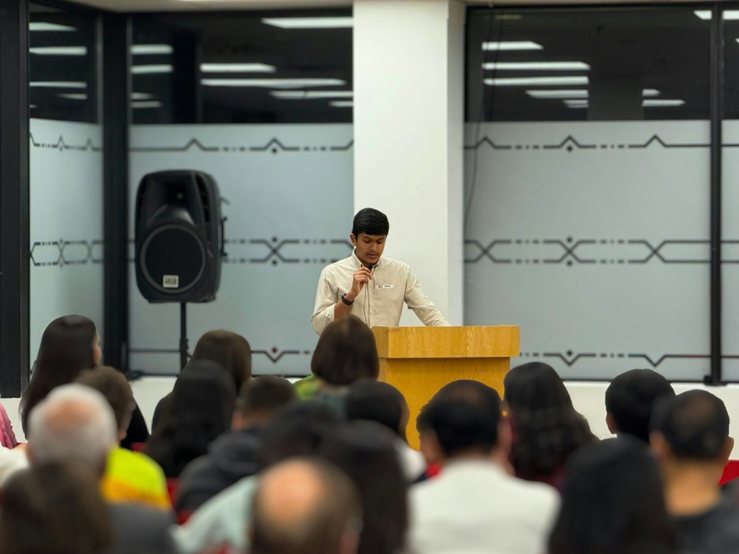Man in a beige shirt speaking into a microphone at a podium.