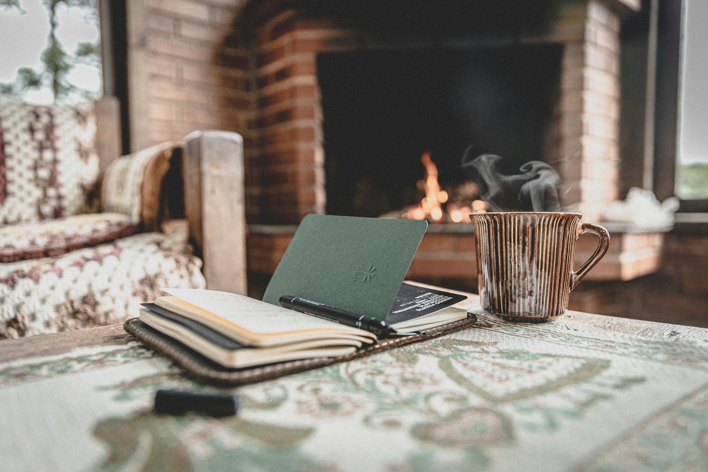 Open journal and steaming mug on a patterned tablecloth.